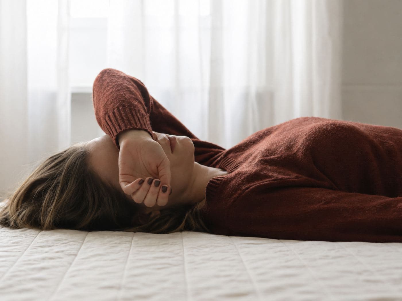 A woman lying on a bed with an arm across her face