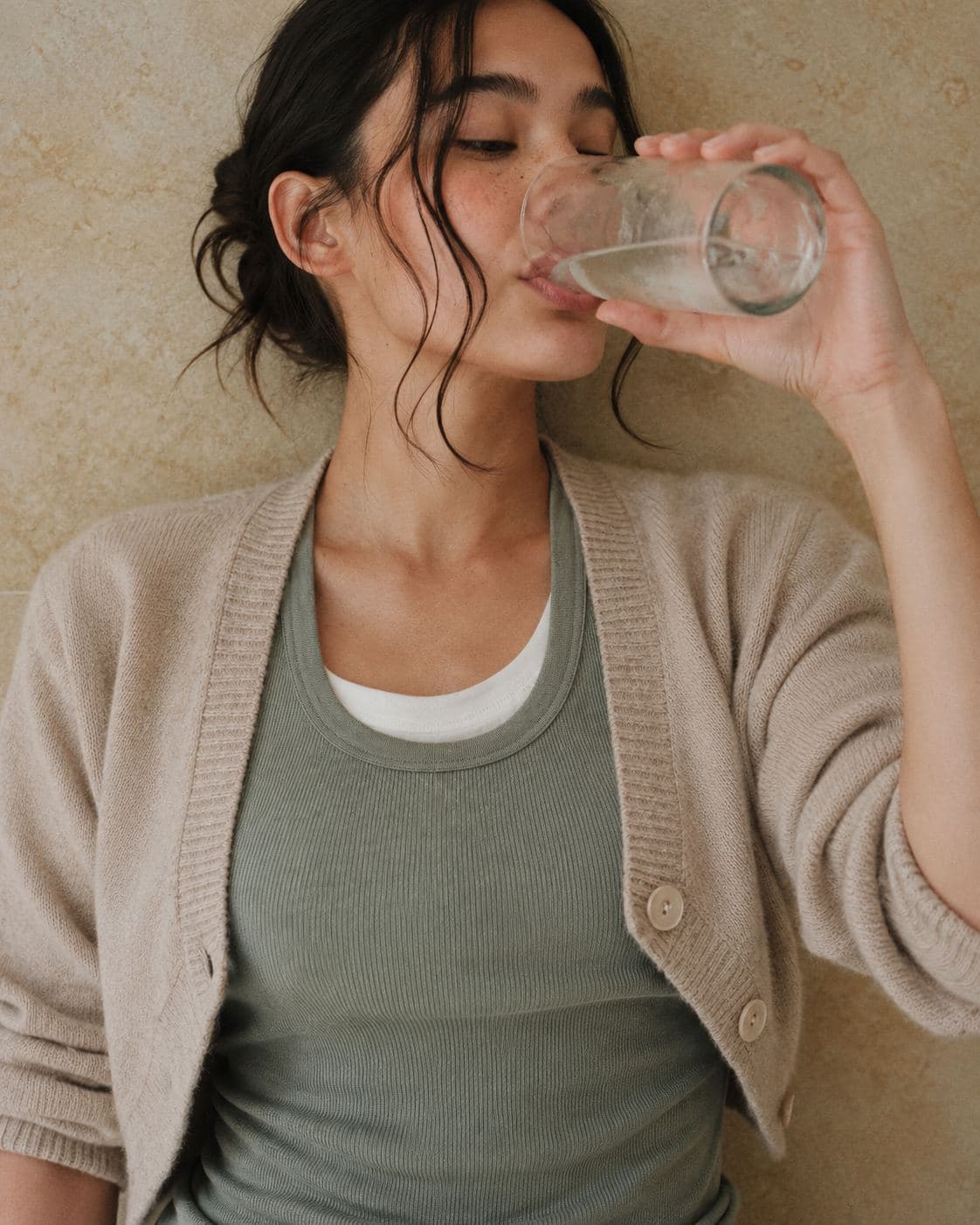 A woman in a beige cardigan drinking a glass of water