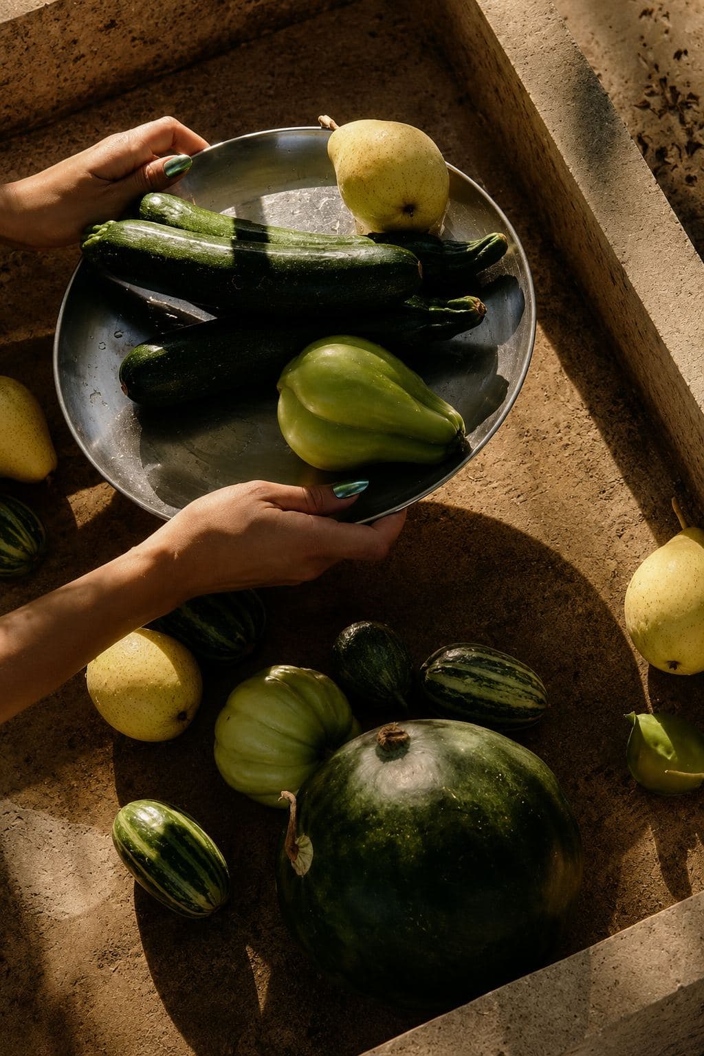 Hands holding a bowl of courgettes and lemons over a rustic table