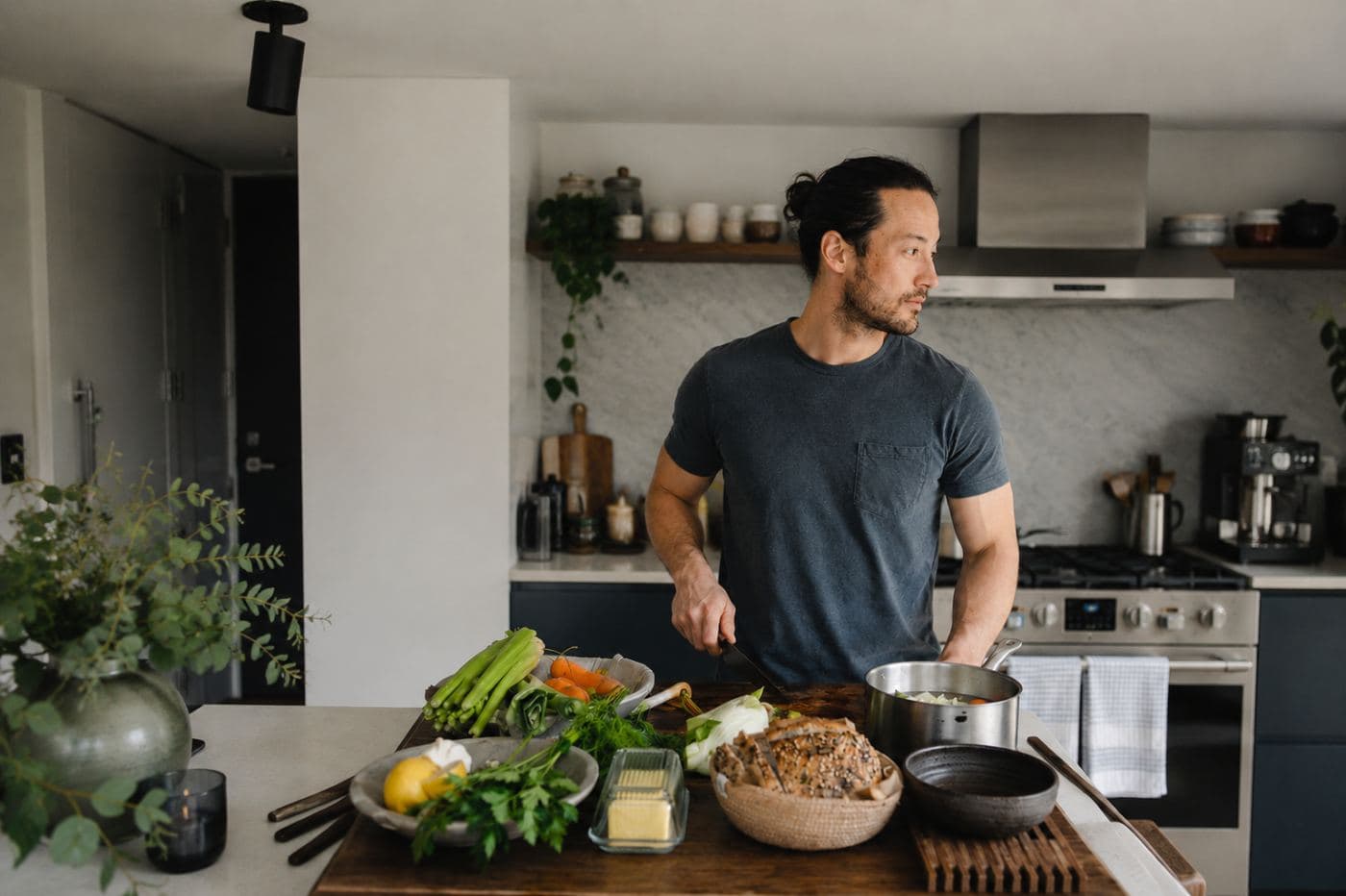 A man cooking in a kitchen with fresh vegetables laid out on the counter